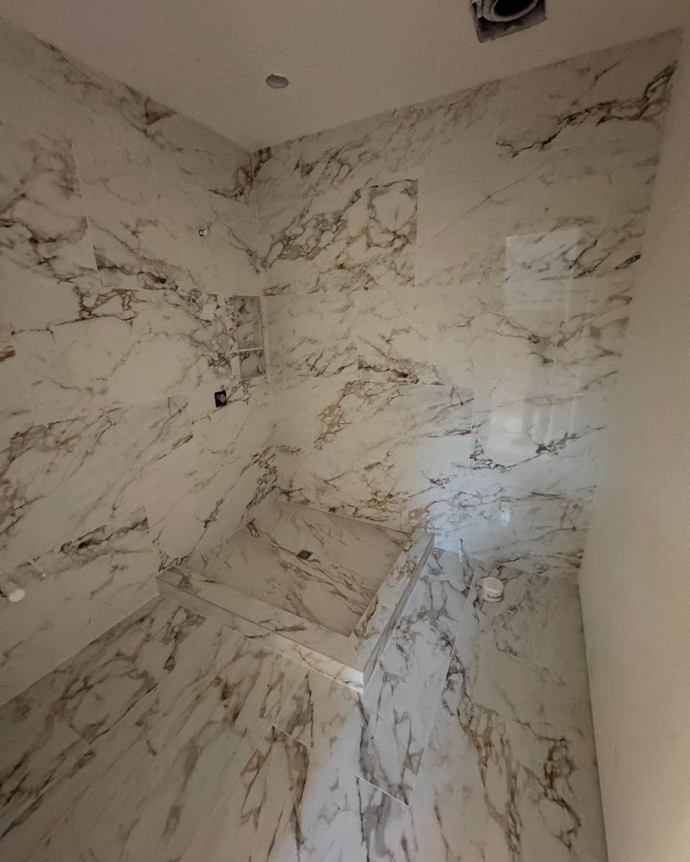 Walk-in shower clad in book-matched white marble slabs with continuous veining across the corner