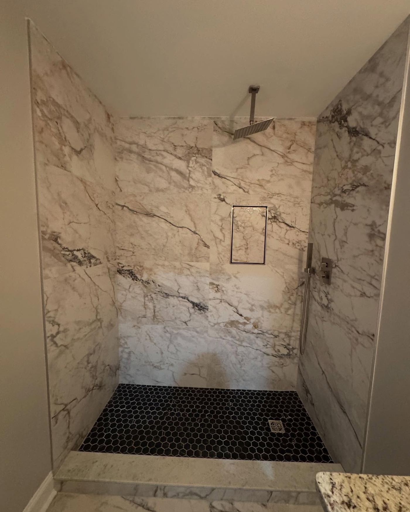 White marble shower with black hexagon mosaic floor and a recessed shampoo niche