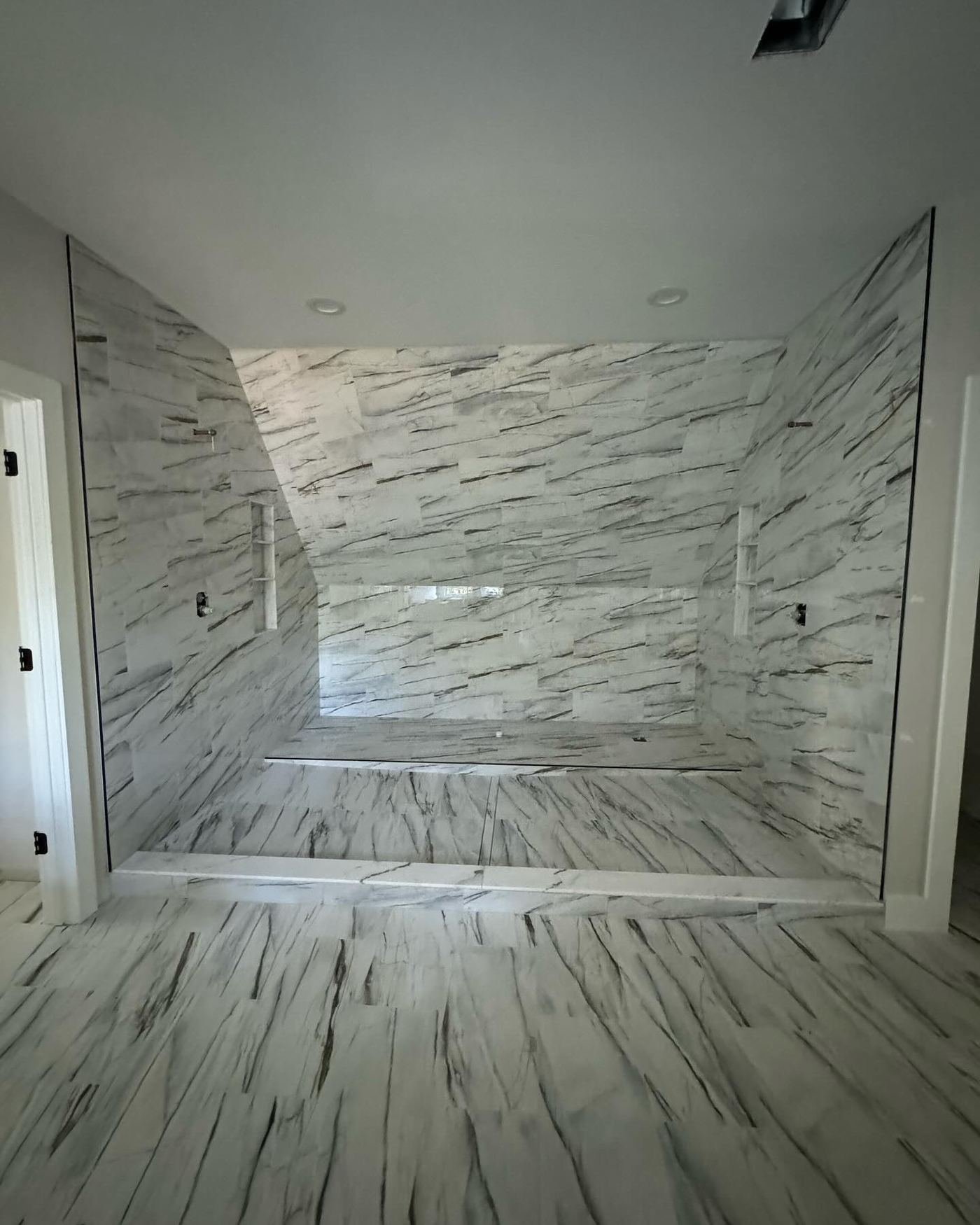 Curbless walk-in shower in veined white and grey marble with a matching stone floor