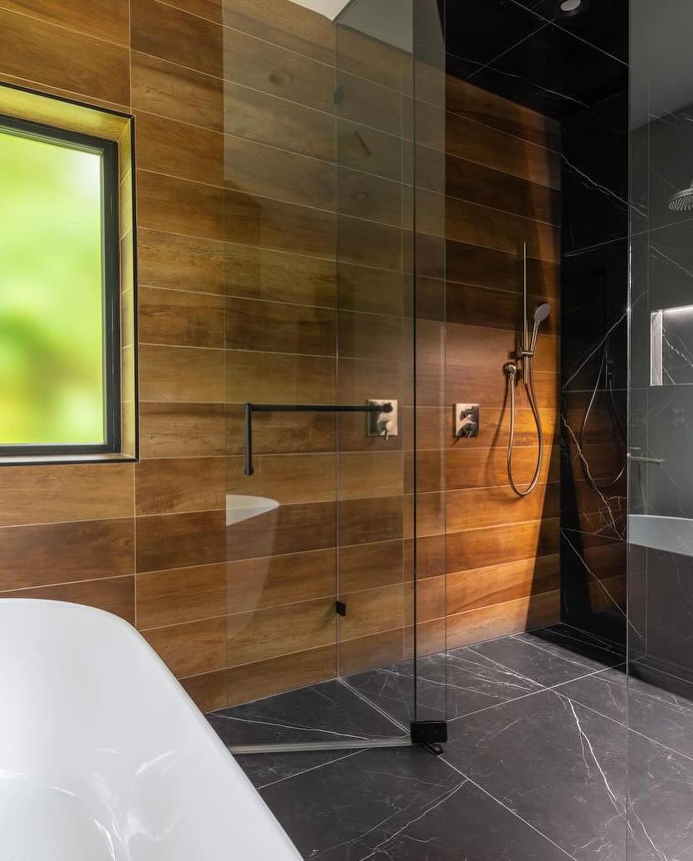 Freestanding tub against a wood-look plank wall beside a black marble glass shower