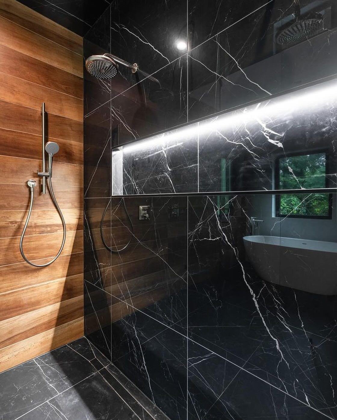 Black marble shower with linear LED lighting, wood-look accent wall and a garden window