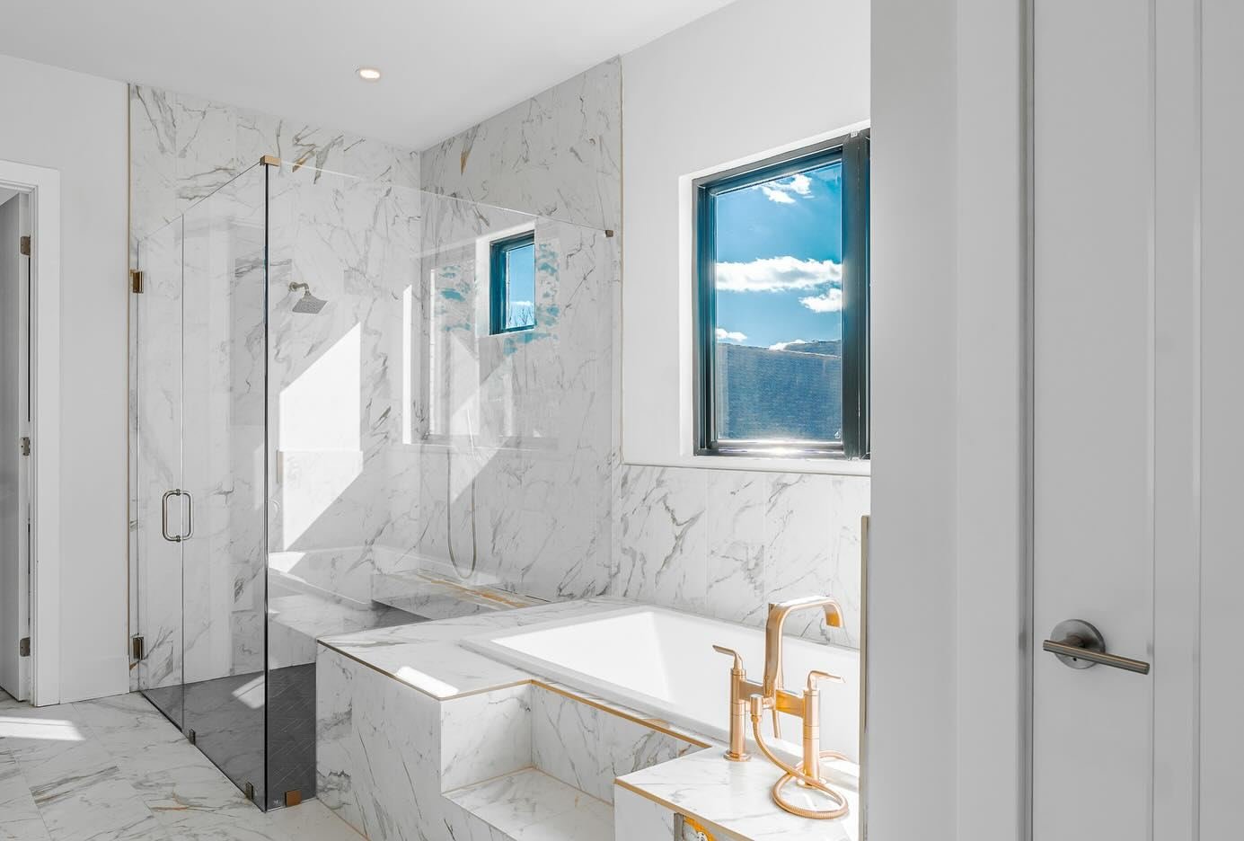 White marble bathroom with a drop-in tub, gold fixtures and a frameless glass shower