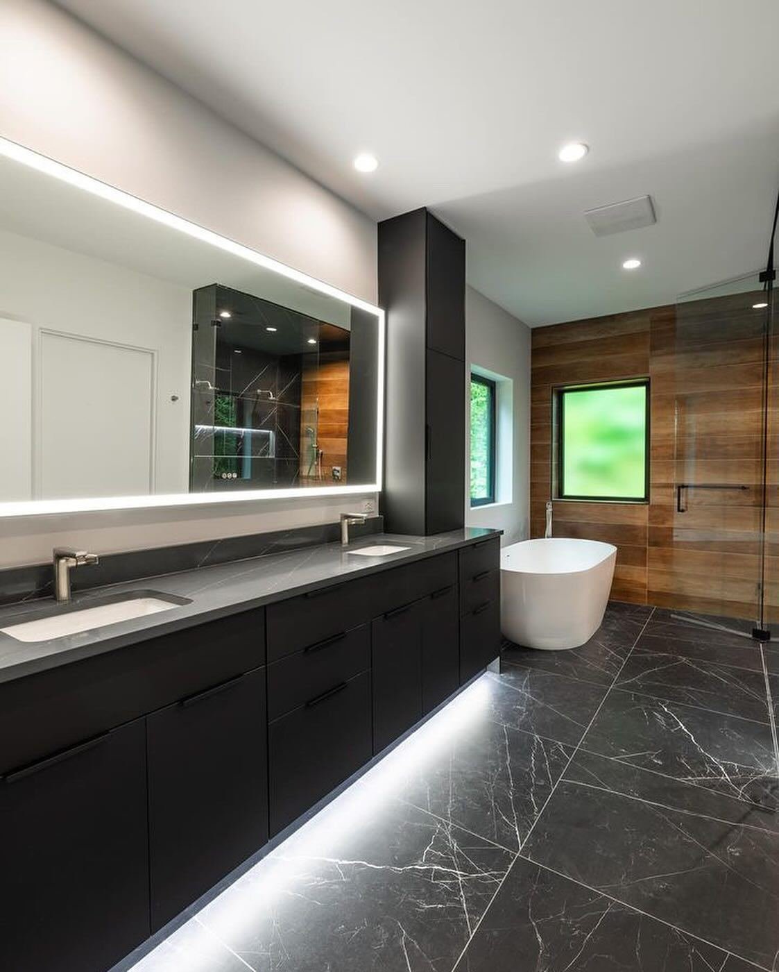 Double vanity with backlit mirror, dark large-format floor tile and a freestanding tub