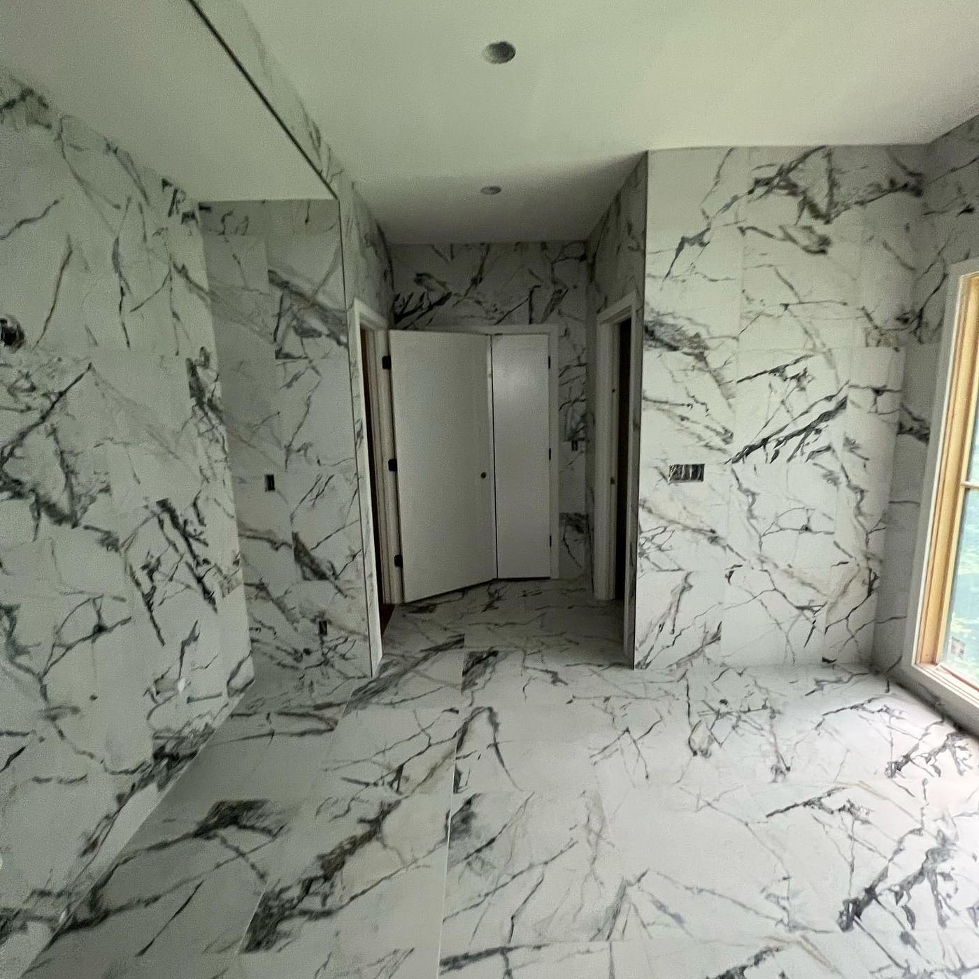 Room lined floor to ceiling in dramatic white marble slabs with grey veining