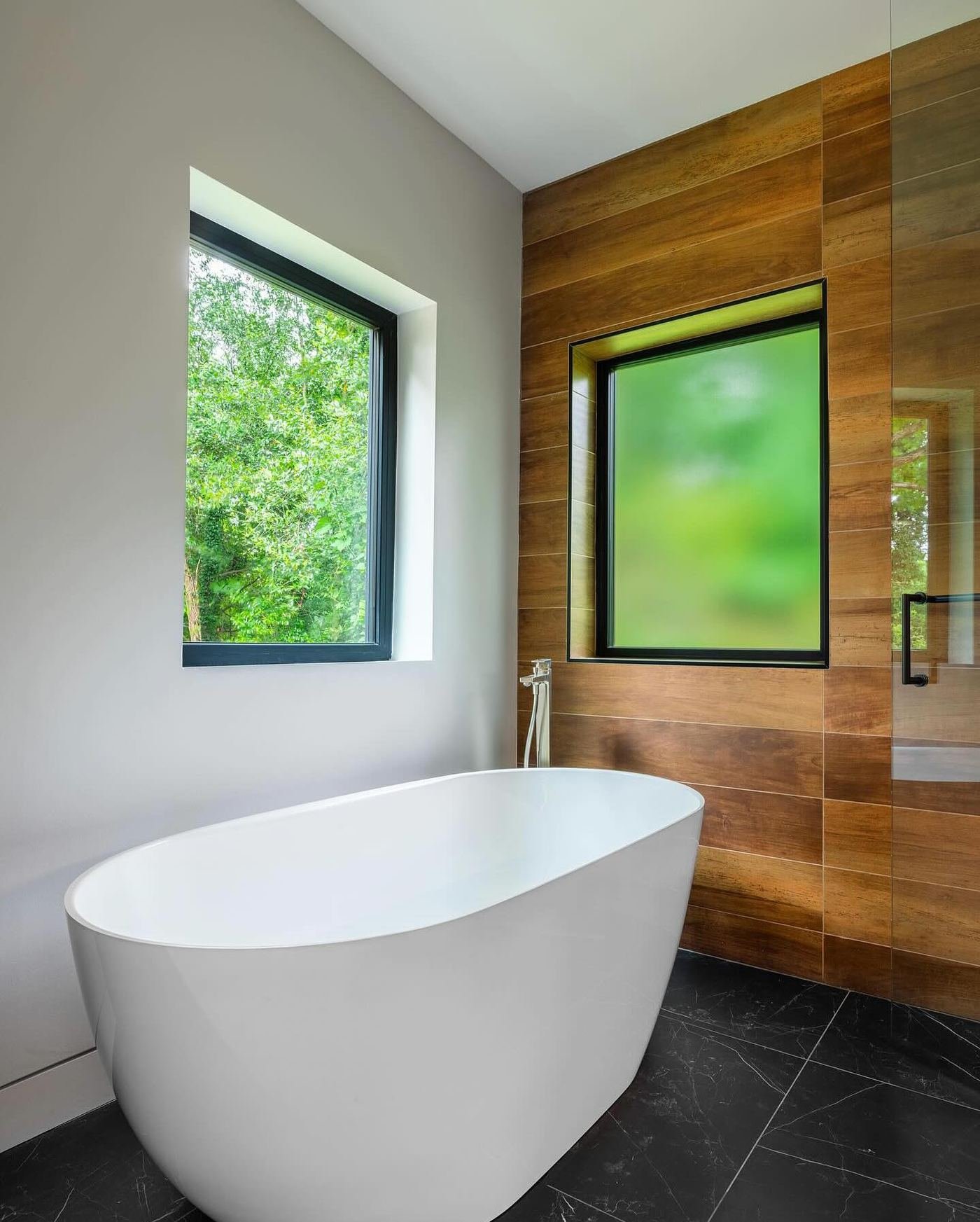 Sculptural freestanding tub against a wood-look plank wall over dark large-format floor tile