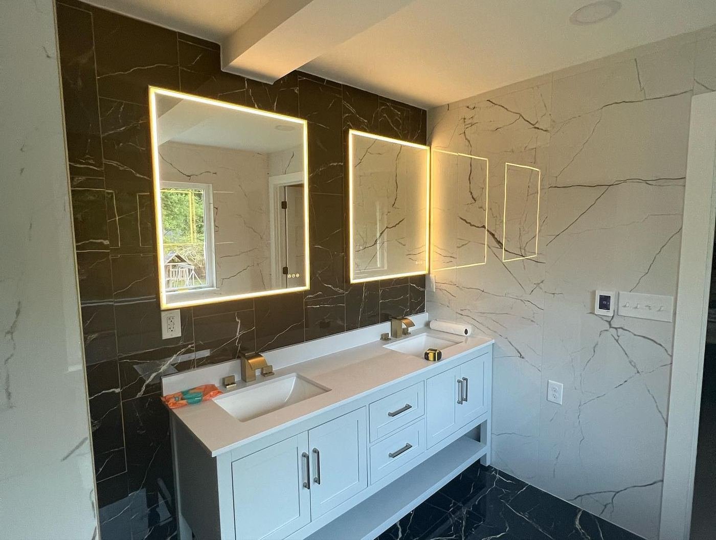 Black marble feature wall behind a double vanity with backlit mirrors