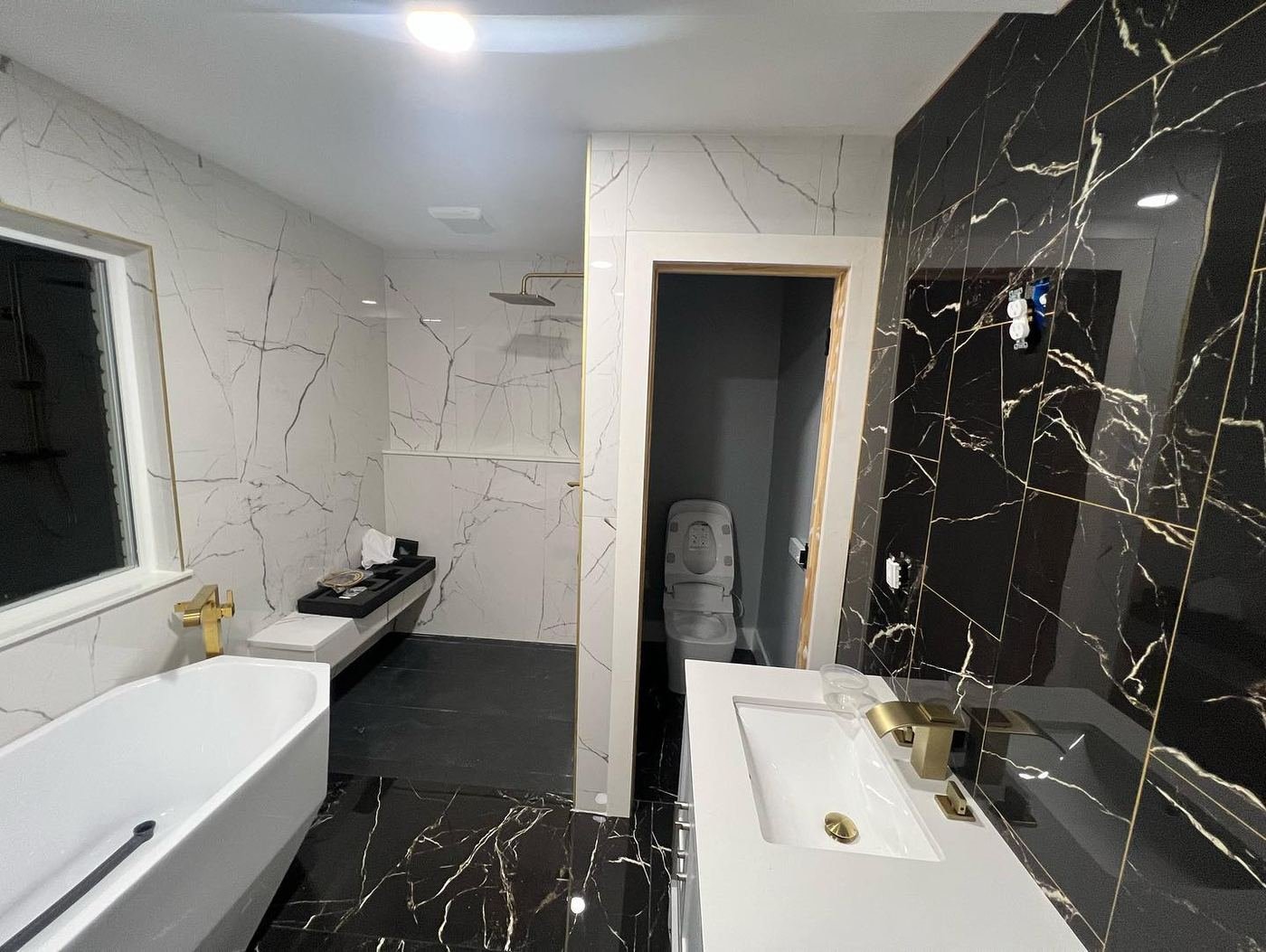 Bathroom pairing a black marble accent wall with white marble, a soaking tub and gold fixtures