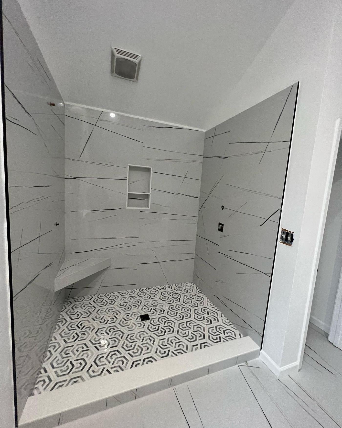 White marble shower with a patterned mosaic floor and a full-height recessed niche