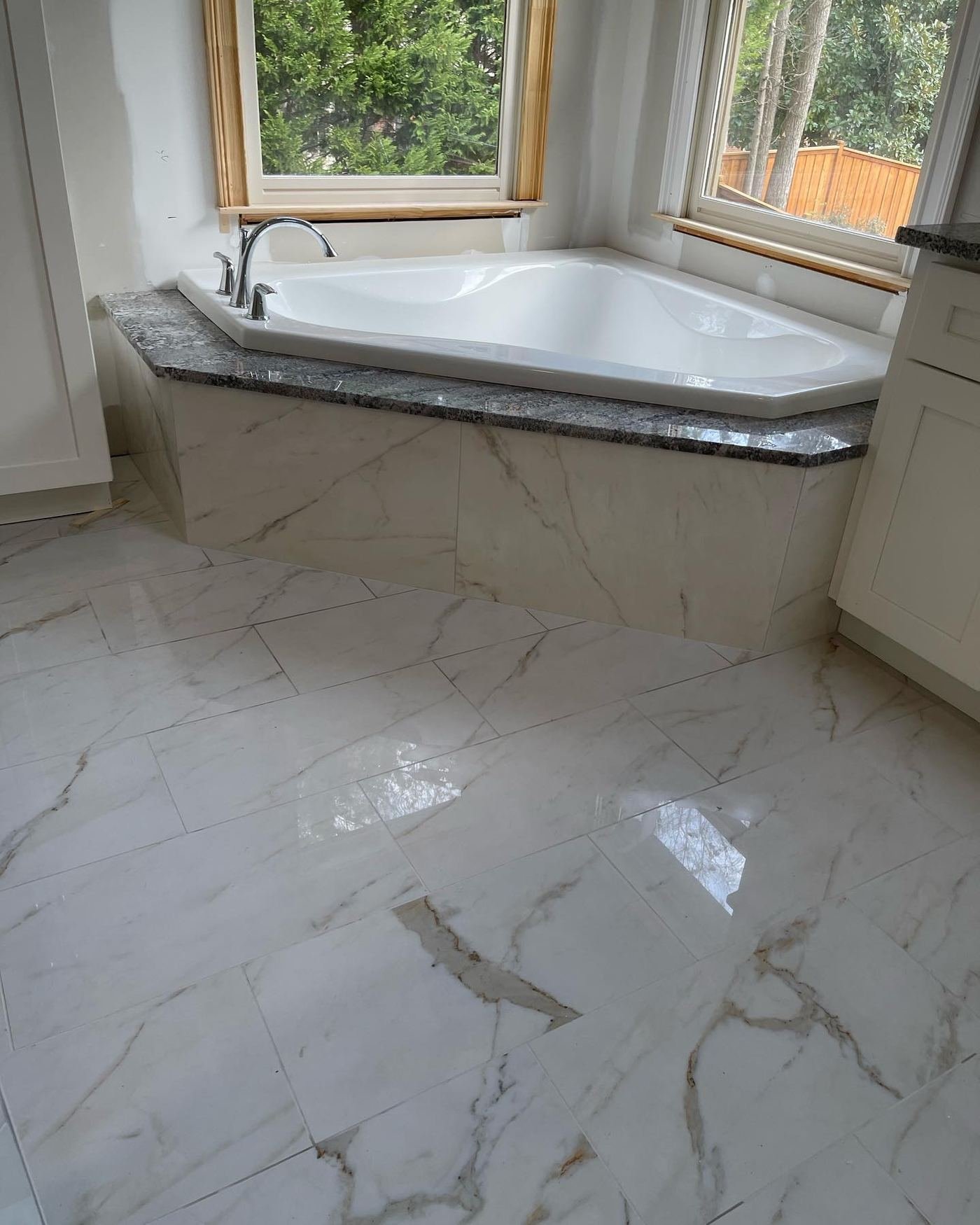 Polished marble floor with a corner drop-in tub set beneath a picture window