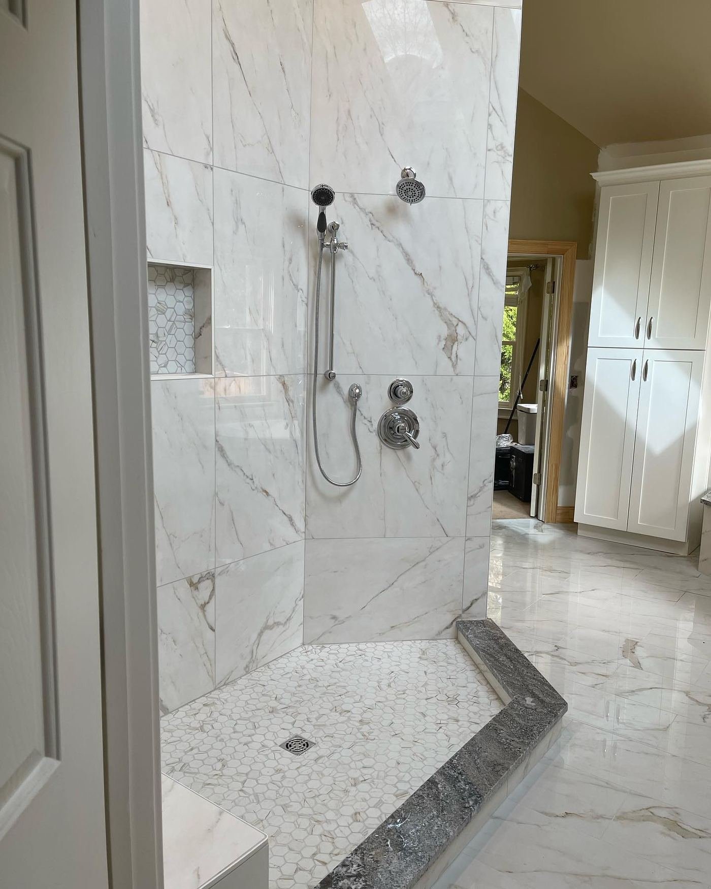Marble shower with a built-in bench, mosaic floor and polished chrome controls