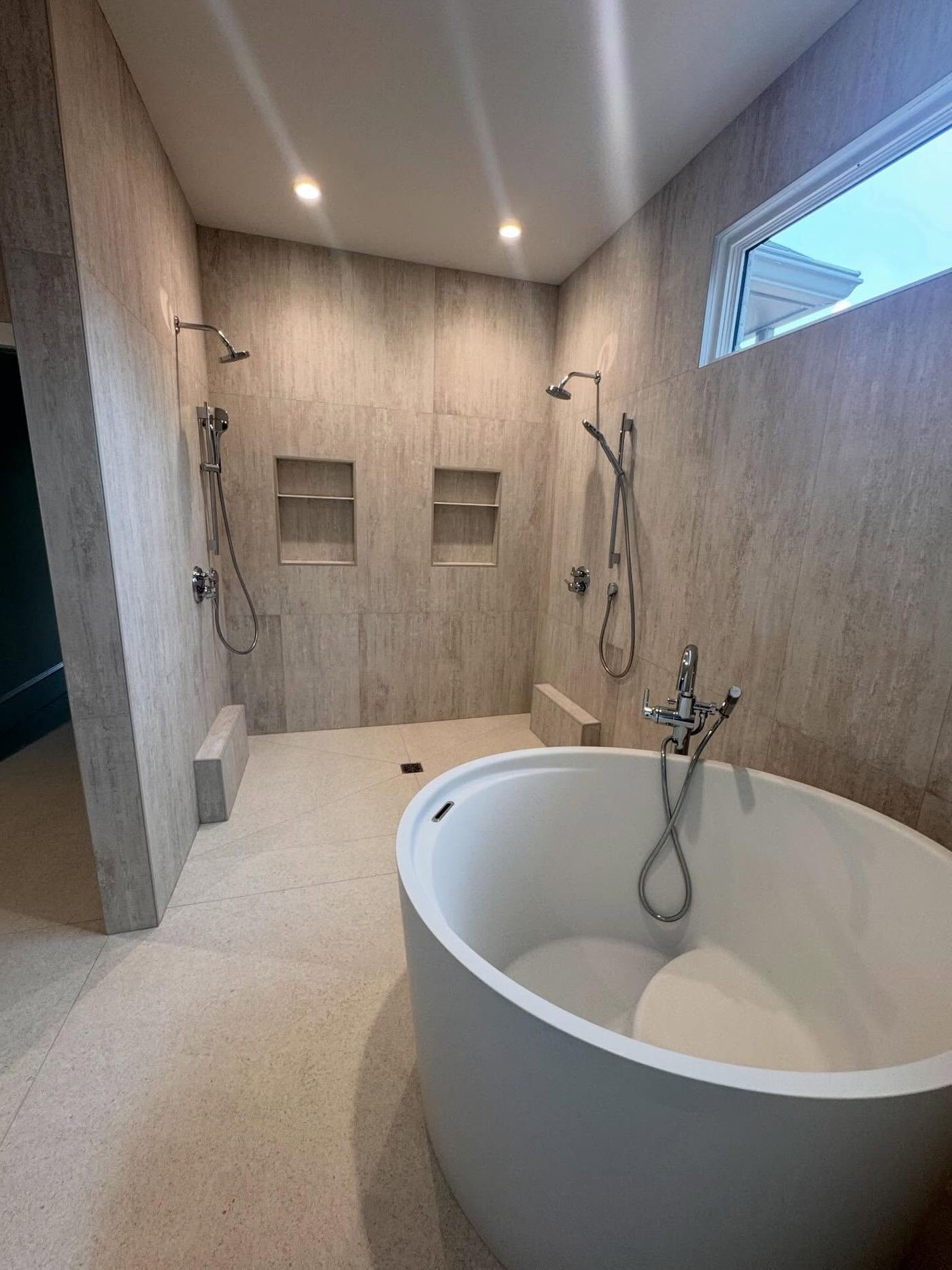 Stone-look wet room with a freestanding tub, hand shower and matching wall tile