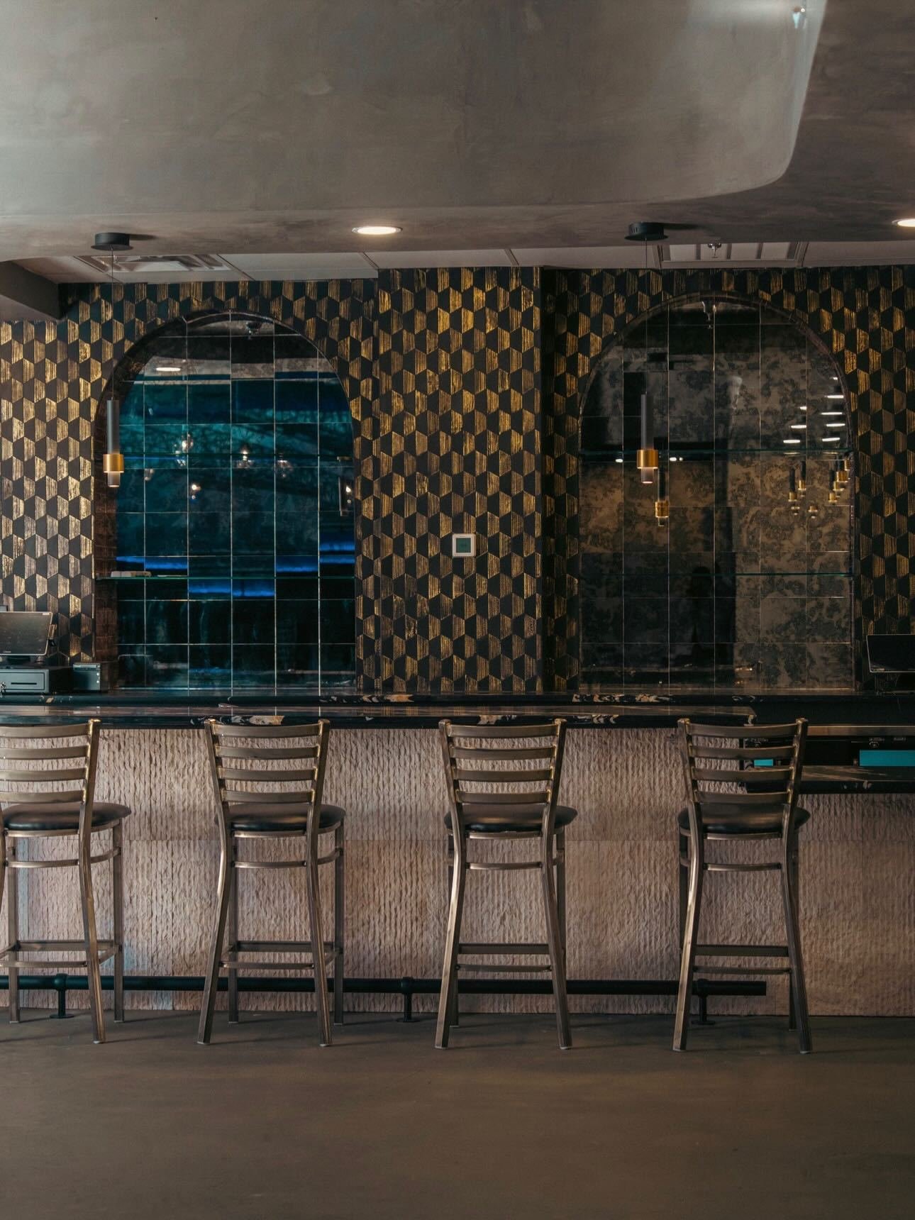 Commercial bar with a geometric gold and teal tile wall and stone counter