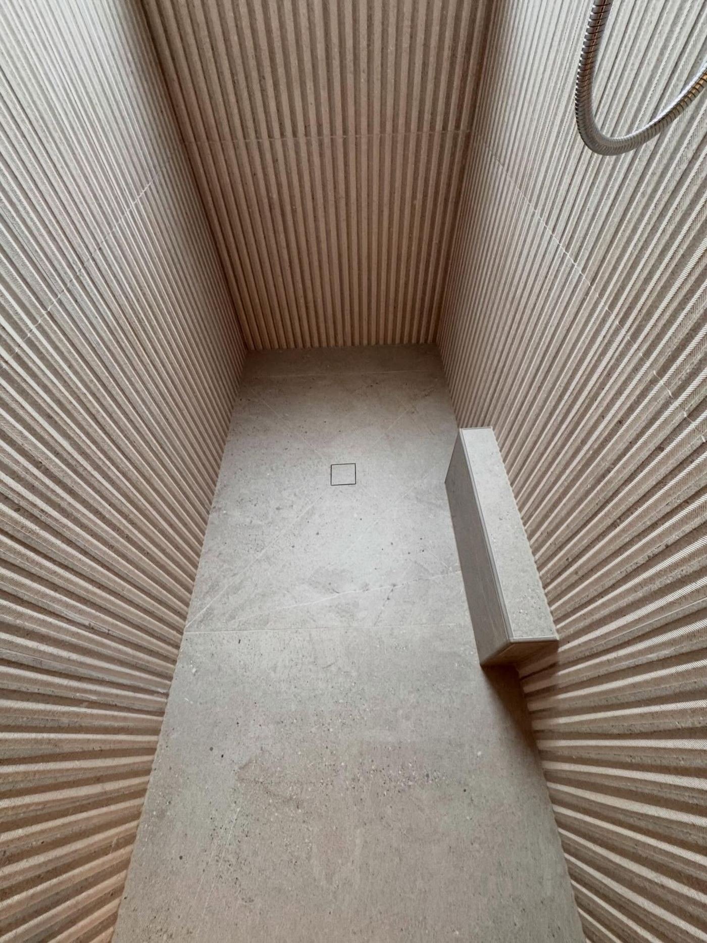 Curbless shower lined in fluted stone with an integrated bench